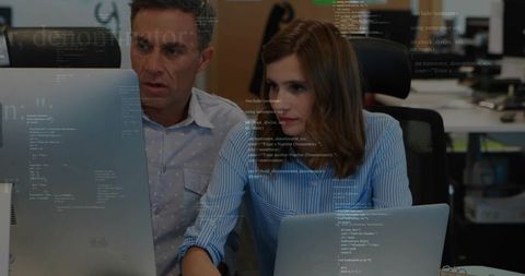 Coworkers Reviewing Code on Monitor and Laptop Pair Programming and Debugging in Office