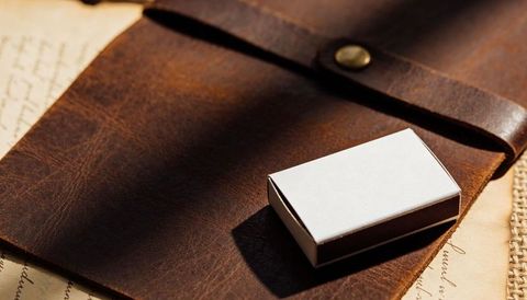 Matchbox casting shadow on leather journal strap with handwritten paper background