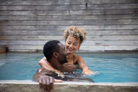 Interracial couple embracing in trendy outdoor pool smiling, relaxing, romantic moment
