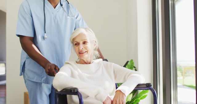 Image of midsection of african american male doctor taking care of caucasian senior woman. seniors health and nursing home lifestyle concept.