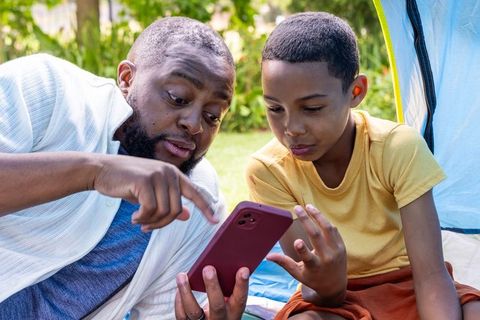 African american father teaching son smartphone skills camping outdoors, family bonding