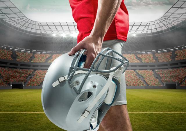 American football player holding silver helmet while standing in large, empty stadium. Ideal for sports promotion, team spirit, game day advertisements, athletic gear marketing, or inspirational sports posters.