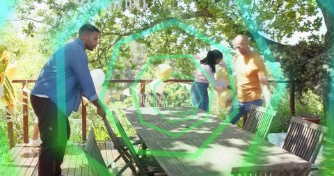 Friends preparing sunlit backyard table for outdoor party with balloons and wooden chairs