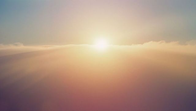 Golden sun above clouds with amber and rose hues at high altitude