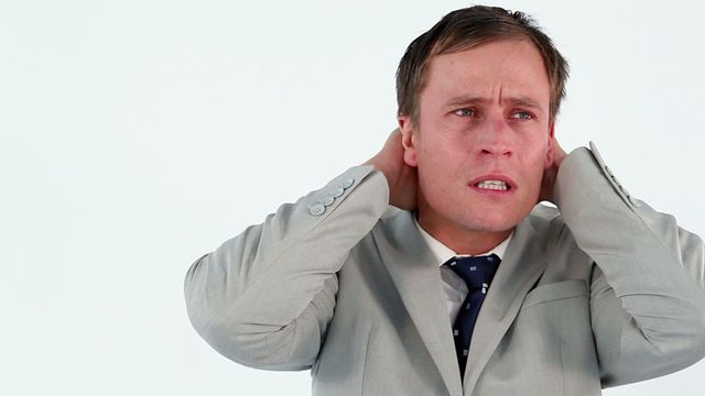 Business professional in a suit expressing stress or frustration against a white backdrop. This is ideal for depicting corporate stress, work-related anxiety, or the challenges of professional life in marketing materials, blogs, or articles discussing business scenarios.