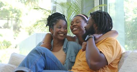 African family relaxing on sofa, parents and teen sharing warm, joyful, cozy moment, smiling