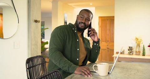 African American man working from home at kitchen island with laptop and smartphone