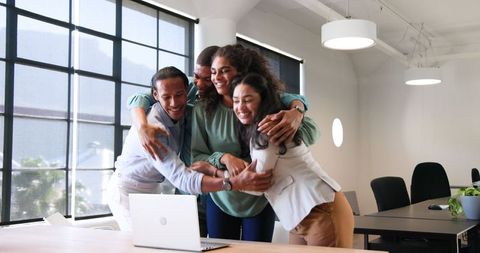 Diverse Team Celebrating Successful Project Around Laptop in Office
