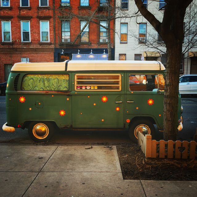 This vintage green Volkswagen van is showcased parked on an urban street. The van features a retro design and is adorned with bright details, all under the soft light of evening. Ideal for themes involving nostalgia, vintage vehicles, urban lifestyle, street photography, and travel adventures.