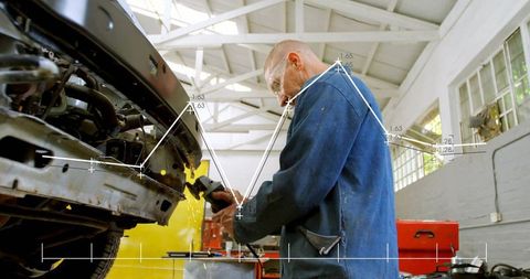 Male mechanic grinding car bumper with digital measuring overlays in bright workshop