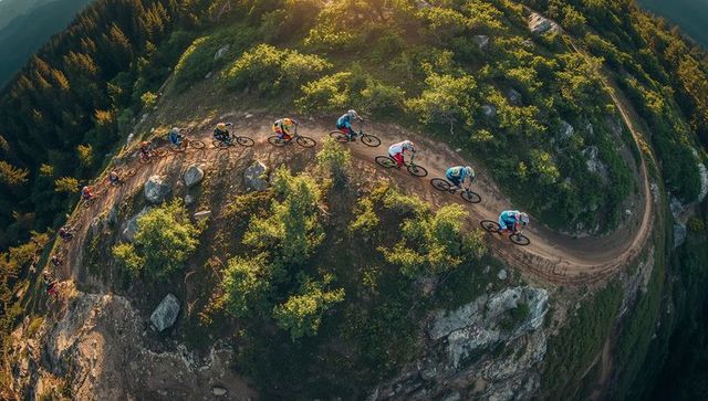Aerial sunset ridge mountain biking team carving narrow singletrack through forest