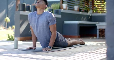 African american man performing upward dog stretch on patio yoga mat with smartwatch