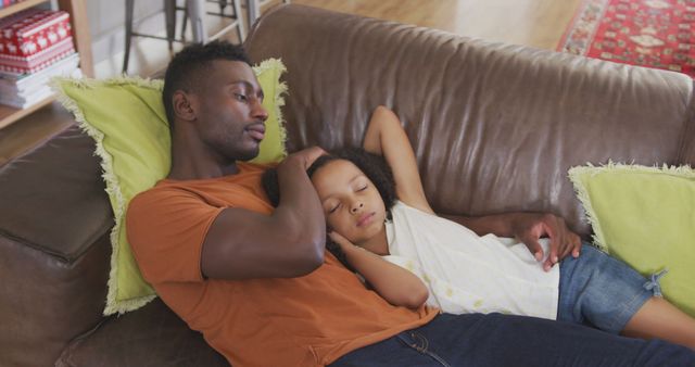 Father and daughter are taking a nap on a brown leather couch in living room. Father is wearing an orange t-shirt and dark jeans while daughter is in casual clothes. Both look comfortable. Great for illustrating family bonding, relaxed home environment, or parenting moments.