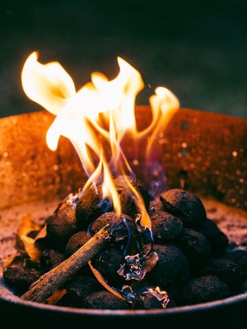 Charcoal briquettes burning with dancing flames in rustic fire bowl for barbecue ambience