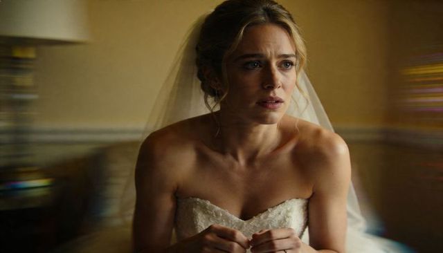 Anxious bride sitting in strapless lace gown clasping hands in bridal suite pre-ceremony
