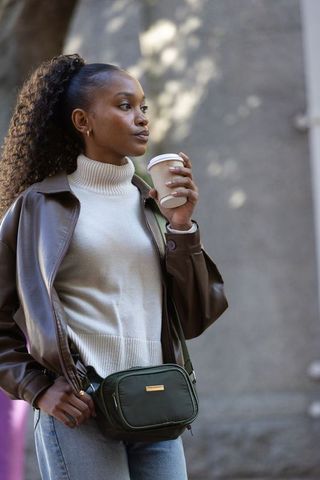 African american woman holding coffee wearing leather jacket and crossbody bag city street