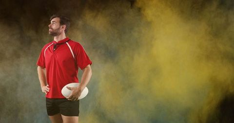 Confident Rugby Player Holding Ball with Intense Smoky Background