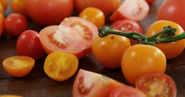 Fresh, ripe tomatoes are sliced and whole on a wooden surface, showcasing the vibrant reds and yellows of the fruit. They represent healthy eating and the simplicity of natural ingredients in cooking.