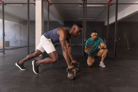 African american athlete doing kettlebell climbers while trainer timing with tablet