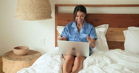 Woman Relaxing in Bed While Using Laptop in Minimalistic Bedroom