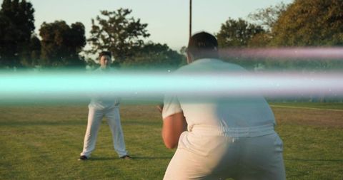 Crouching wicketkeeper preparing catch on sunset park field with dramatic lens flare