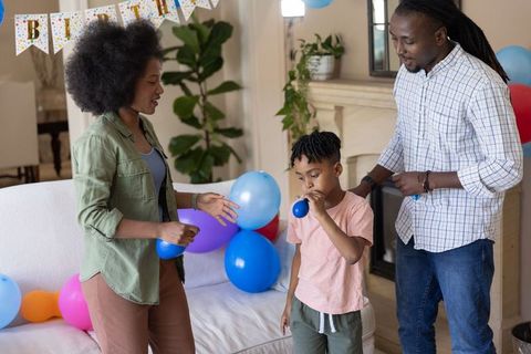 African american family celebrating birthday at home with child blowing blue balloon