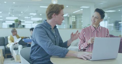 Two colleagues collaborating and discussing project in modern open office lounge with laptop