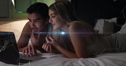Couple lying on bed watching laptop late night cozy intimate moment sharing screen