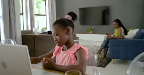 African american mother and daughter working and learning at home with laptop and phone