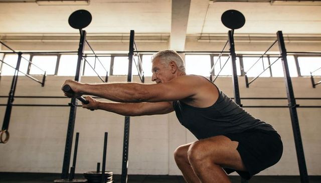 Senior man squatting holding bar in industrial gym training strength and focus
