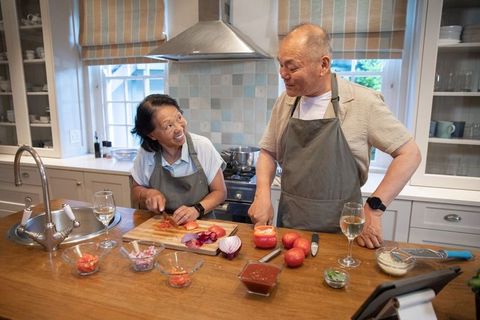 Senior chinese couple cooking together in bright contemporary kitchen chopping tomatoes