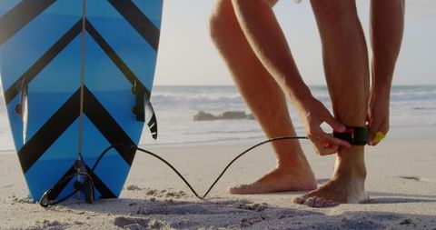 Surfer preparing board leash on sunny beach