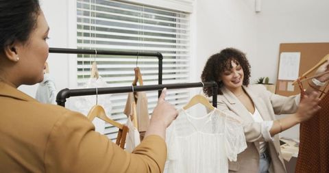 Boutique coworkers styling dresses and discussing wardrobe choices in bright showroom