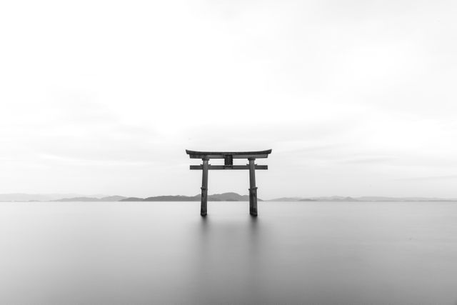 Japanese Torii gate standing in calm water under tranquil sky, exuding a sense of peace and mindfulness. Ideal for use in design projects focused on spirituality, mindfulness, culture, travel experiences related to Japan or zen-inspired artworks.