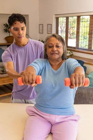 Personal trainer assisting senior with dumbbell workout at home