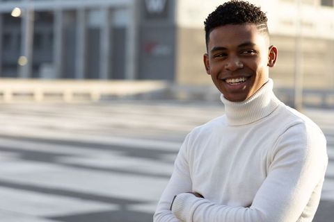 Smiling confident african american teen standing on urban plaza wearing white turtleneck