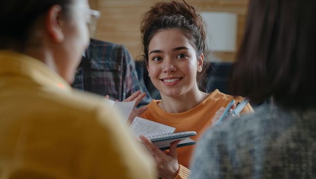 Smiling teen girl studying with friends in cozy wooden lounge holding spiral notebook