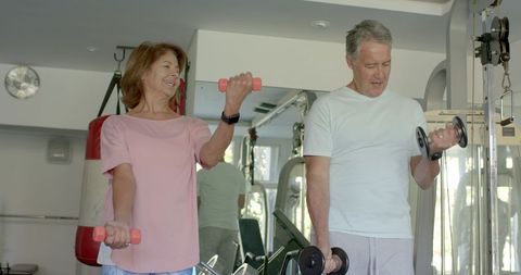 Active Senior Couple Lifting Dumbbells at Gym
