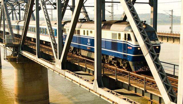 Blue-and-white passenger train crossing massive steel truss bridge over wide river