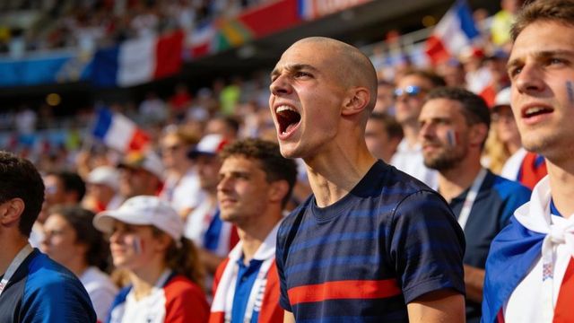 Bald fan shouting in packed stadium surrounded by french flags and passionate supporters