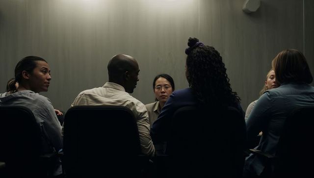 Asian leader facilitating diverse team discussion in dim boardroom, focused collaboration