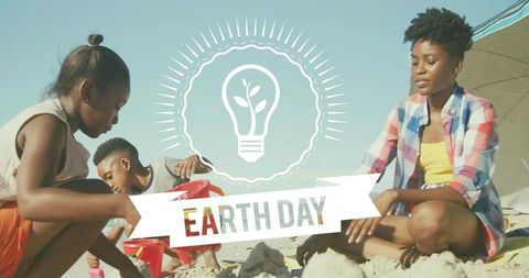 Family Building Sandcastles on Beach for Earth Day Celebration with Eco Lightbulb Banner