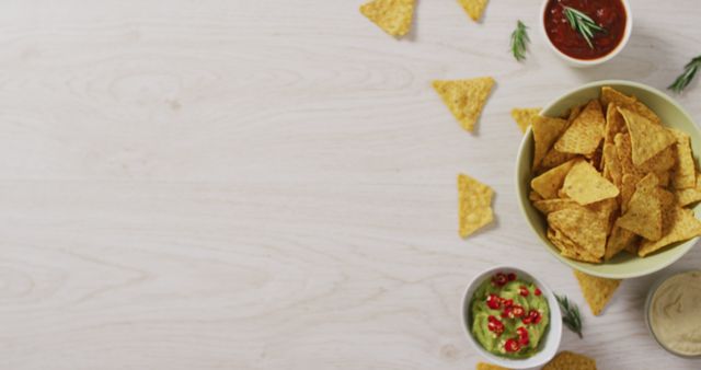 Image of tortilla chips, guacamole and salsa dip on a wooden surface. party food and savoury snacks.
