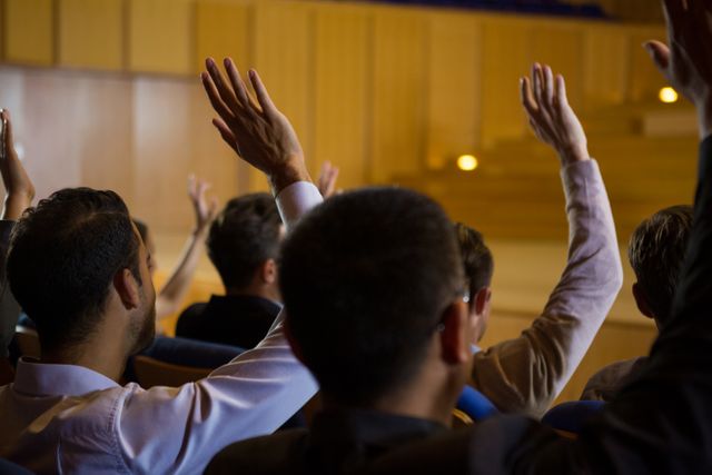 Business executives raising hands during a conference, indicating active participation and engagement. Ideal for use in materials related to corporate training, seminars, workshops, professional development, and business meetings.