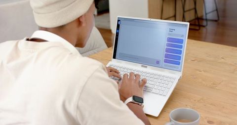African american man typing on laptop for remote work at home wearing beanie and smartwatch