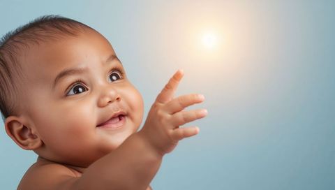 Smiling Infant Reaching Toward Warm Glow on Soft Blue Background, Close-Up Studio Portrait