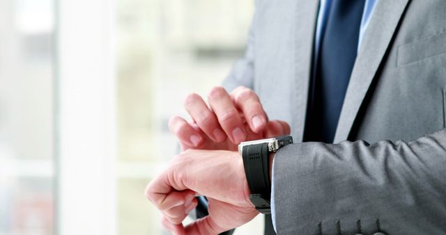 Businessman adjusting a wristwatch in a modern office. Ideal for use in articles, presentations, websites, and advertisements focusing on professionalism, corporate settings, time management, success, or punctuality.