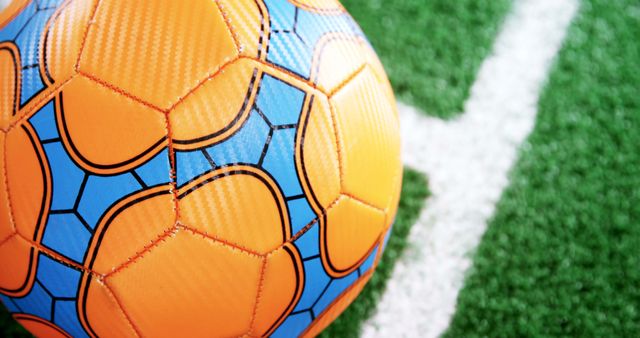 A close-up view of a colorful soccer ball on a green artificial turf field, with copy space. Its vibrant colors and the texture of the turf convey the energy and excitement associated with soccer games and sports events.