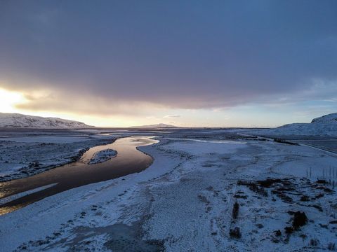 Golden sunrise reflecting on snow-covered river winding through frozen winter plain