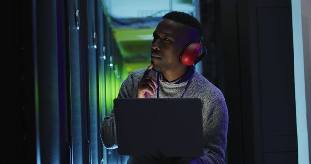 IT professional working in a server room, analyzing the data on a laptop while wearing ear protection. Ideal for visuals related to technology, data management, cybersecurity, IT support, and network administration.